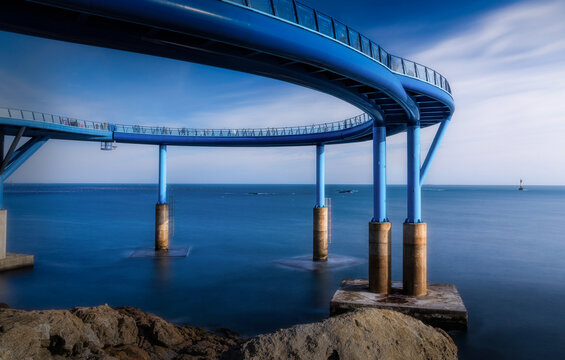 View of the graceful, ultramarine curved skywalk arches over the serene, silky ocean, a modern marvel against the rocky coast, Busan, Busan, South Korea.