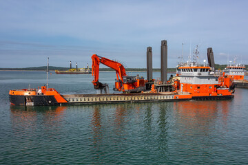 Large Dredging Vessel with Excavator Working in Harbor. Marine Construction Barge Performing Seabed Dredging for Port Development and Industrial Waterfront Projects