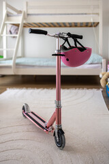 Child's pink kick scooter and safety helmet in a cozy bedroom. Concept for active childhood, outdoor recreation, and sports safety for kids.