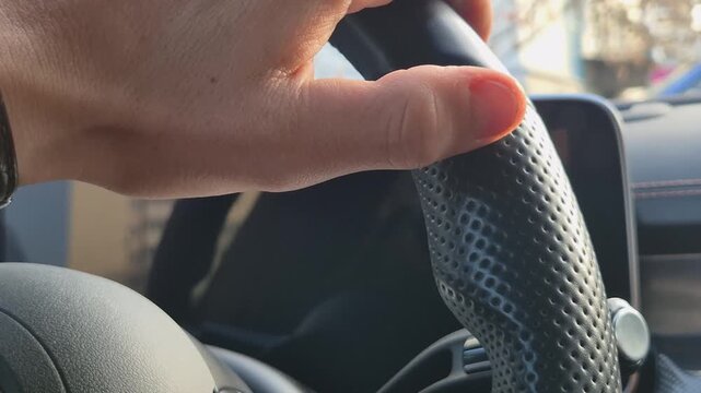 The driver's hand touching the pleasant perforated leather material of the steering wheel