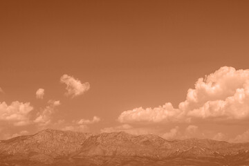 Mountains stand under a cloudy sky at dusk with a warm orange tint during the late evening hours