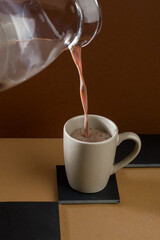 Hot drink is poured from a jar into a cup placed on a black surface