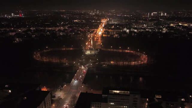 Luftaufnahme von Friedensengel in Muenchen, Deutschland bei Nacht. Beleuchtete Strassen, Prinzregentenstrasse, Luitpoldterrasse, Bogenhausen, Korinthische Saeule, goldene Statue, Stadtansicht.