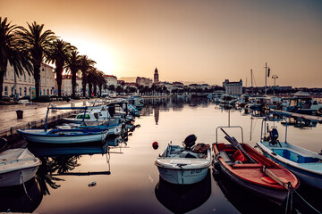 View of boats gently bobbing in the tranquil harbor waters as the sun casts a warm glow over the ancient city skyline, Split, Split-Dalmatia County, Croatia.