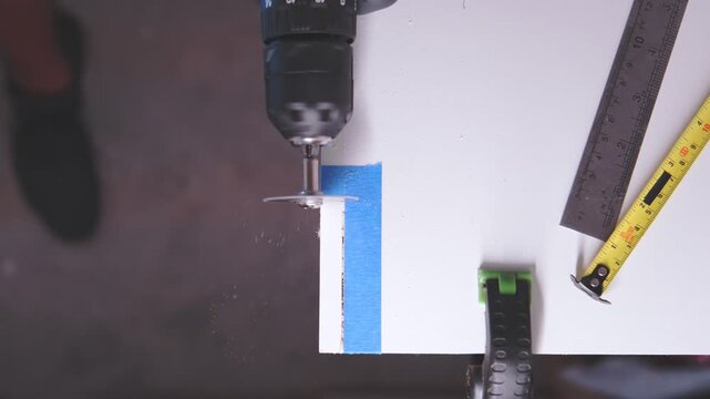 Close-up of a worker using a circular saw attachment on a drill to cut a white wooden board - Powered by Adobe