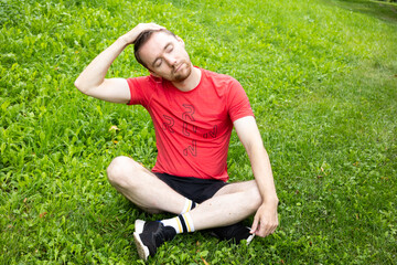 European sporty man stretching his neck on the green grass in the park in summer
