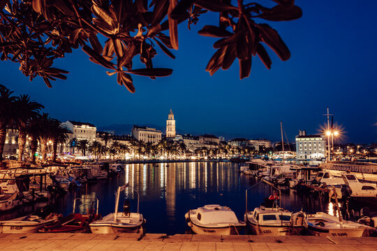 View of the city lights shimmer on the still harbor waters, reflecting off the boats nestled close to the shore at night, Split, Split-Dalmatia County, Croatia.