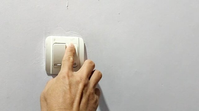 A finger pressing a light switch on a wall inside symbolizes power, control, energy conservation, or daily routines at home. The concept of energy.
