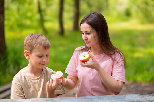 Mother and son eating apples, smiling and sharing fruits in park