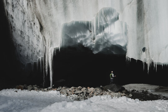 View of a solitary figure stands amidst the stark beauty of a glacial cave, framed by icy daggers and rocky terrain, Morteratsch Glacier, Pontresina, Grisons Canton, Switzerland.