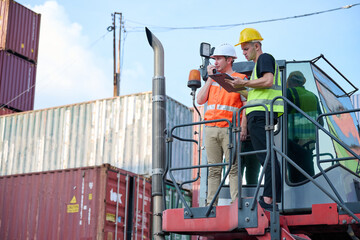 Workers discussing their project plan in containers yard. They are wearing hard hats and safety vests