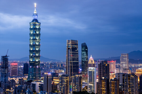 View of Taipei 101 piercing the twilight sky amidst a cluster of modern skyscrapers, its illuminated spire contrasting against the darkening horizon, Taipei, Taiwan.