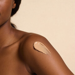 swatch of beige cream on dark skin women, macro texture of the skin on which the cream is applied	