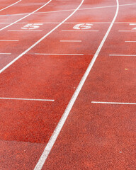 Fototapeta premium Red running track marked with lanes and numbers shows space for athletes practicing or training during a sunny day
