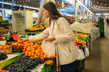 Woman selecting fresh oranges at a colorful fruit market stand. Healthy lifestyle and food shopping routine.