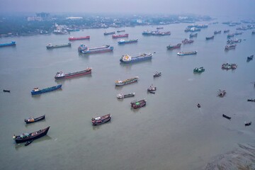 Aerial view of a waterway bustling with ships of varying sizes and colors, creating a vibrant mosaic against the muted water, Chattogram, Chittagong Division, Bangladesh.