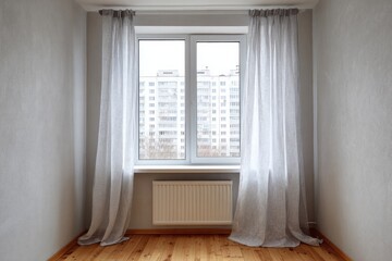 Unfurnished room interior features a white window with sheer gray curtains and a radiator below