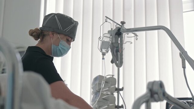 Professional female nurse in medical mask adjusting intravenous drip system, healthcare worker managing patient treatment in bright hospital ward room