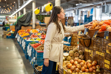 Woman shopping for fresh produce at a local indoor market. Choosing healthy vegetables and fruit during grocery run.