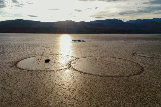 Aerial view of sun reflecting off the cracked earth and circular patterns on the desert floor, with mountains in the background, Alvord Desert, Princeton, Oregon, United States.