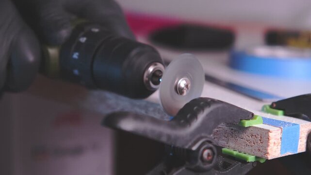 Close-up of a worker cutting a clamped wooden board with a rotary tool in a workshop