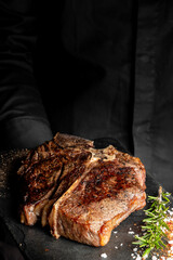 A pan-seared T-bone or porterhouse steak on a dark serving board with rosemary and coarse salt.