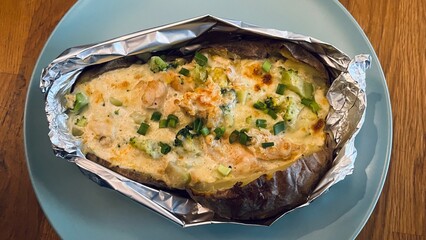 Foil baked potato filled with melted cheese, vegetables and shrimp, topped with green onions. Warm homemade meal, rustic food style and casual dining.