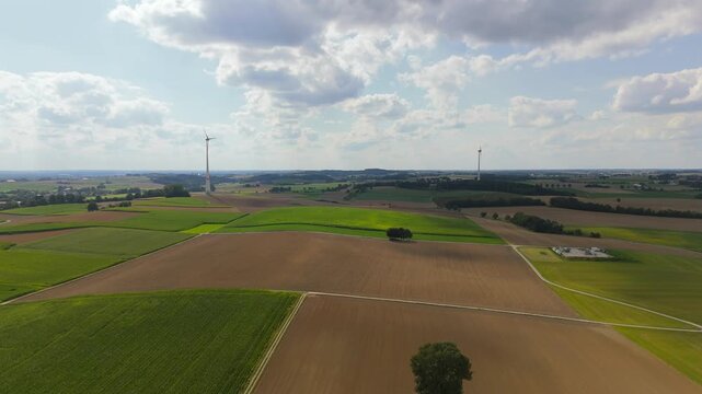 Drone shot over German farmlands with prominent wind turbines on the horizon. Symbolizes renewable energy, green technology, sustainable development, and clean power generation