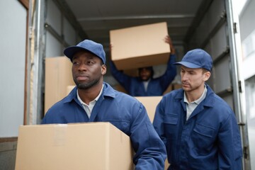 Diverse male movers unloading boxes from truck