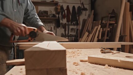 Skilled Craftsman Demonstrates Precision Woodworking Techniques Using a Handsaw to Cut Lumber in a Well-Equipped Workshop with Tools and Wood Shavings