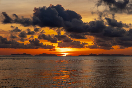 View of the tranquil sea reflecting the fiery sunset, with dark clouds contrasting against the vibrant orange sky, Phi Phi Island, Krabi, Thailand.
