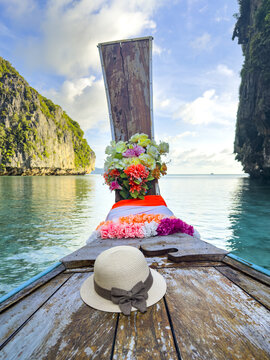 View of a traditional longtail boat adorned with vibrant flowers and a sunhat gliding through turquoise waters framed by towering limestone cliffs, Phi Phi Island, Krabi, Thailand.