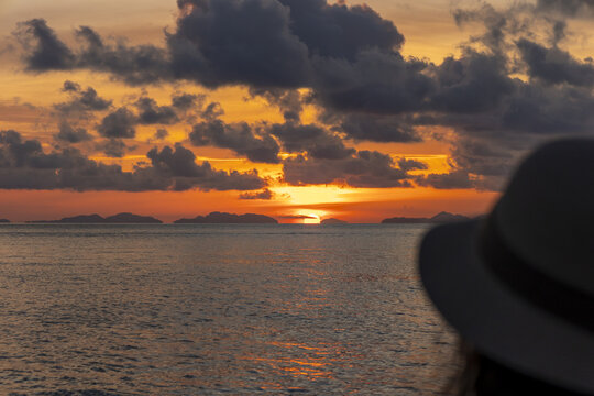 View of a golden sunset casting a warm glow on the tranquil sea, dotted with distant islands under a cloudy sky, Phi Phi Island, Krabi, Thailand.
