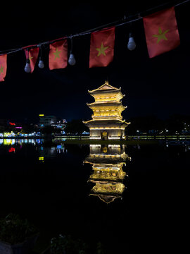 View of a glowing pagoda reflected in dark water under a string of red Vietnamese flags at night, Hoa Lư, Ninh B&igrave;nh, Vietnam.