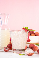 Lychee fruit tasty margarita or lemonade cocktail. Tasty alcohol drink with fresh lychees, mint leaves, liqueur and sweet sour juice, on white pink table background with ripe raw lychee fruits, copy s