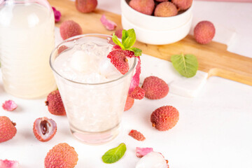 Lychee fruit tasty margarita or lemonade cocktail. Tasty alcohol drink with fresh lychees, mint leaves, liqueur and sweet sour juice, on white pink table background with ripe raw lychee fruits, copy s