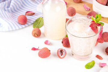 Lychee fruit tasty margarita or lemonade cocktail. Tasty alcohol drink with fresh lychees, mint leaves, liqueur and sweet sour juice, on white pink table background with ripe raw lychee fruits, copy s