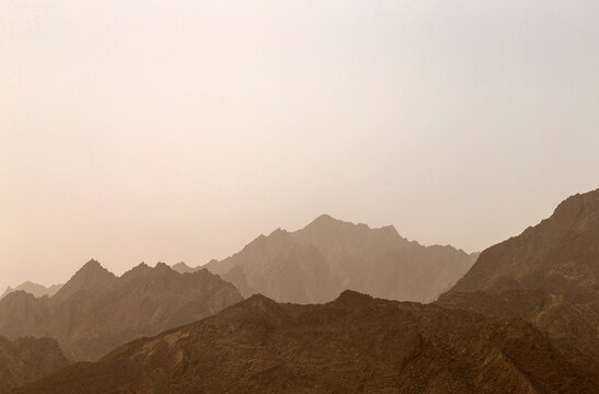 View of rugged, brown-hued mountains rise against a soft, hazy sky, creating a serene yet imposing scene, Makran Coastal Highway, Balochistan, Pakistan.