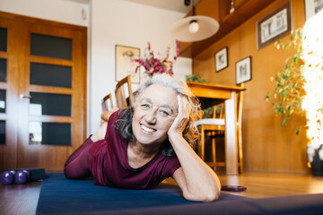 Happy mature woman practicing yoga on a mat in her living room