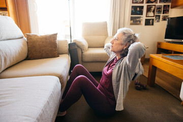 Senior woman exercising core muscles doing a sit-up in her living room