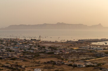View of a serene coastal scene with boats dotting the water and buildings nestled along the shore, under a hazy sky, Gwadar, Balochistan, Pakistan.