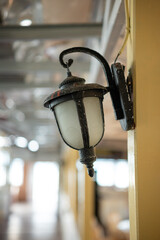 Classic style wall lamp mounted on building pillar with blurred interior background.