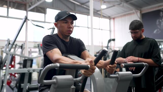 Muscular man training his back muscles on a row machine with a personal trainer supervising