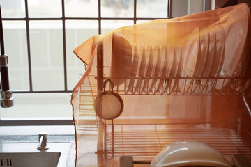 Clean dishes are neatly arranged on a drying rack and covered with a gauze cloth to protect them from insects or dust. White plates of various sizes are drying next to the sink after washing.