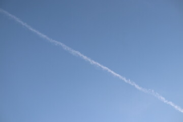 Long white jet contrail cutting diagonally across a clear bright blue sky background