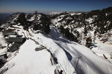 View of a snow-covered landscape with a winding path and scattered buildings, bathed in the soft glow of winter light, Nathia Gali, Khyber Pakhtunkhwa, Pakistan.