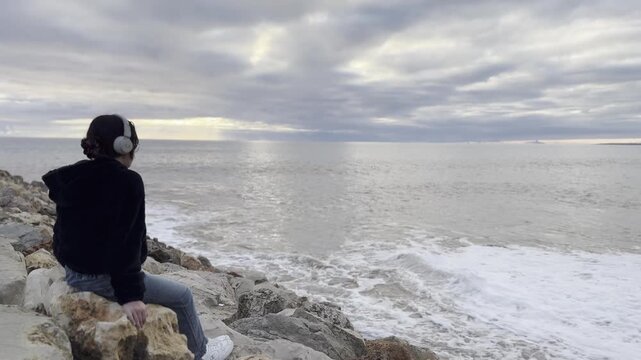 Teenager girl in yellow jacket sitting on a rock and looking at stunning nature background with ocean and cliffs. Travel and tourism. portugal. Dramatic sunset sky. Famous area.