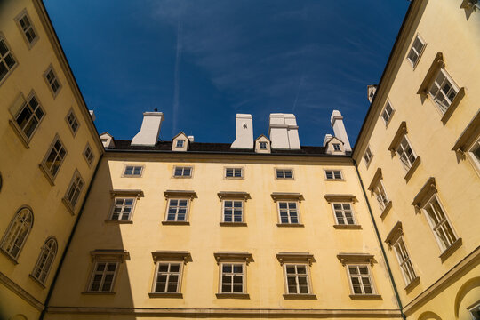 View of the light yellow building with rows of symmetrical windows reaching towards the clear blue sky above, Vienna, Vienna, Austria.