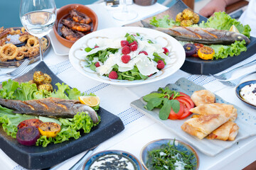 Seafood dishes, including grilled sea bass, calamari, shrimp, and appetizers, arranged on an elegant restaurant table, offering a delicious mediterranean dining experience