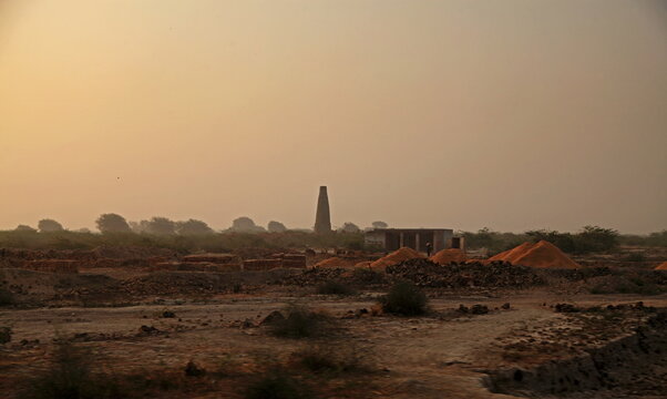 View of piles of bricks scattered across the arid landscape under a muted sky, with a tall chimney standing in the distance, Mithi, Sindh, Pakistan.